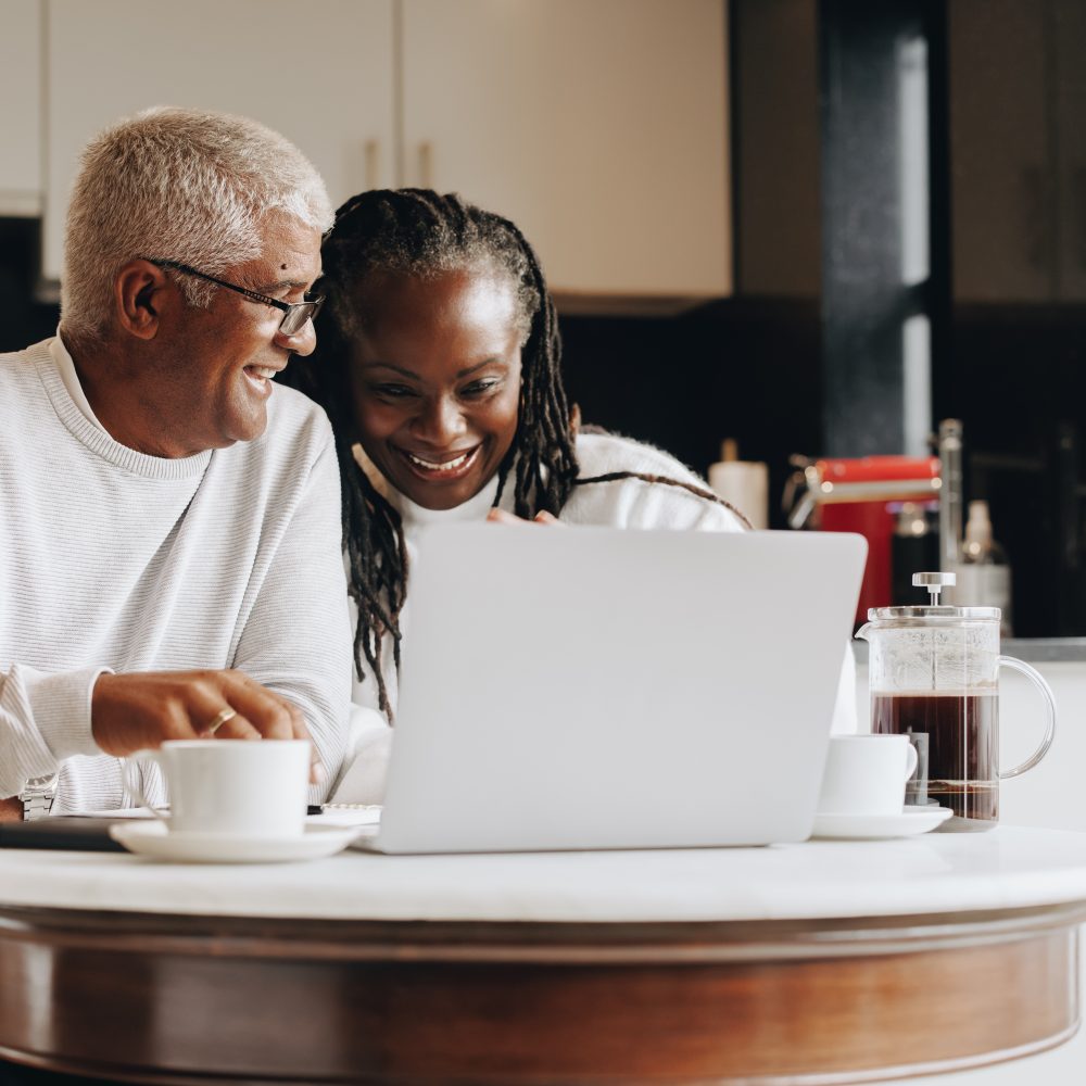 Happy senior couple having a video call on a laptop at home. Mature couple having a virtual meeting with a retirement consultant. Ethnic senior couple planning their retirement together.